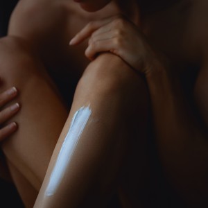 Woman applying white nourishing cream on shin leg. Close-up of shins and knees. Body care